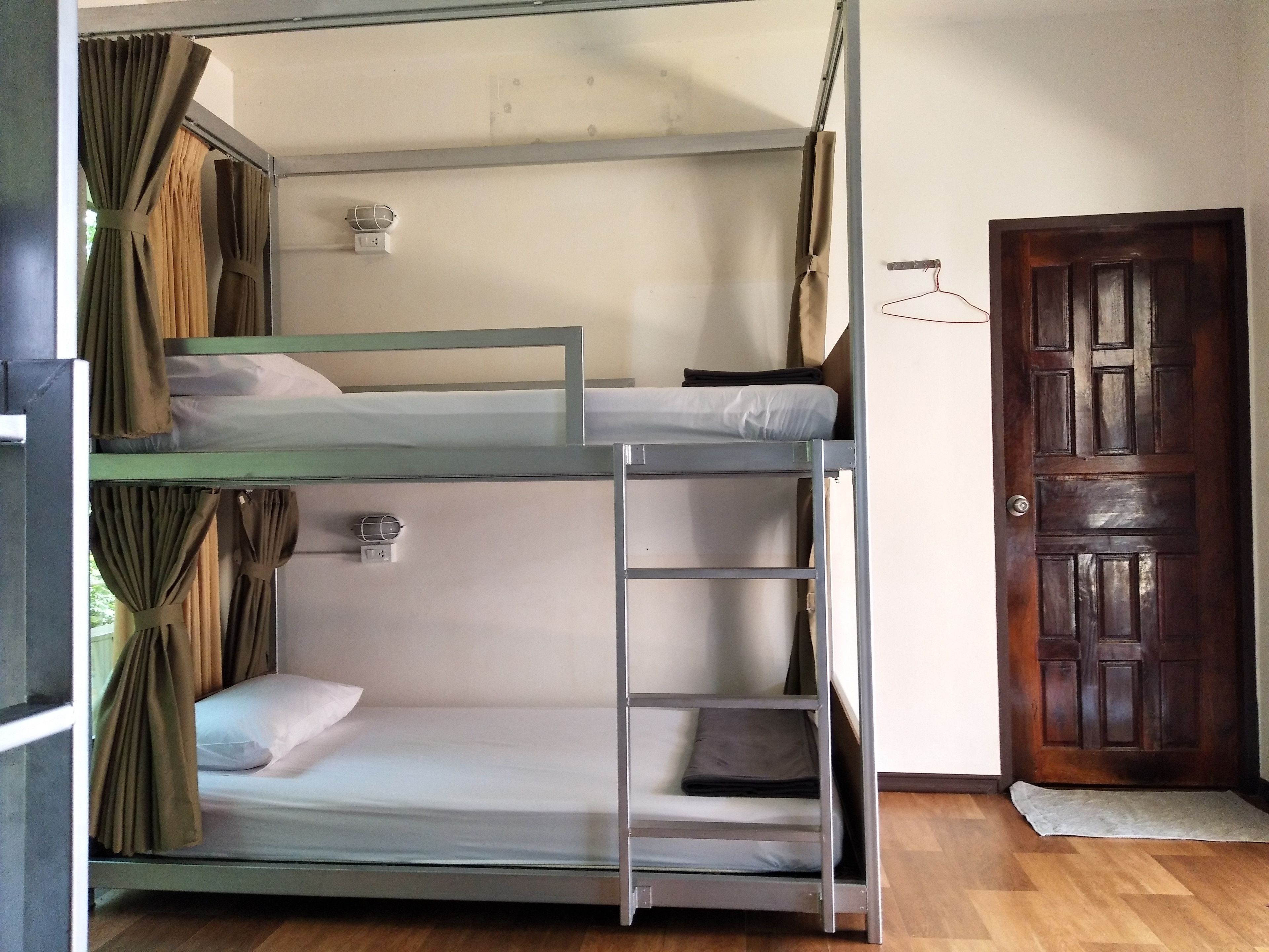 Habitación con literas, una puerta de madera, una mesita y una cortina.