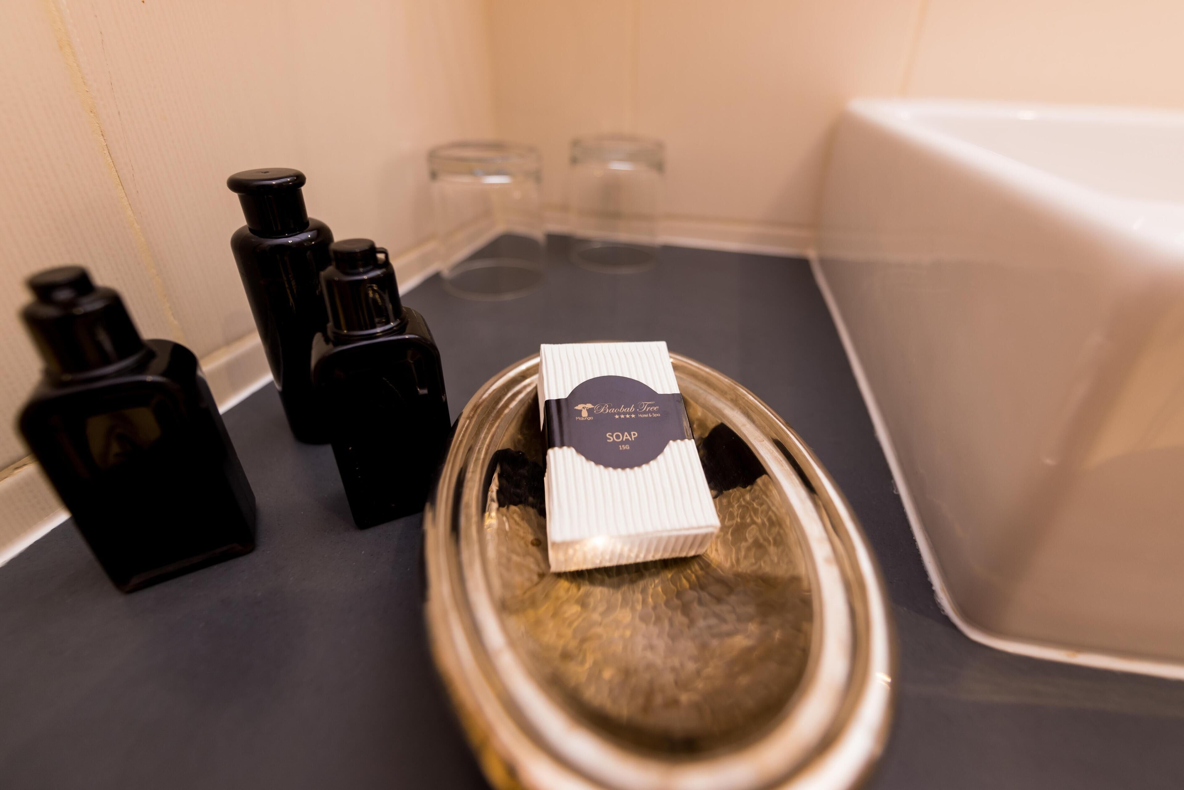 A bathroom counter with a soap dispenser, a bottle, and a glass container.