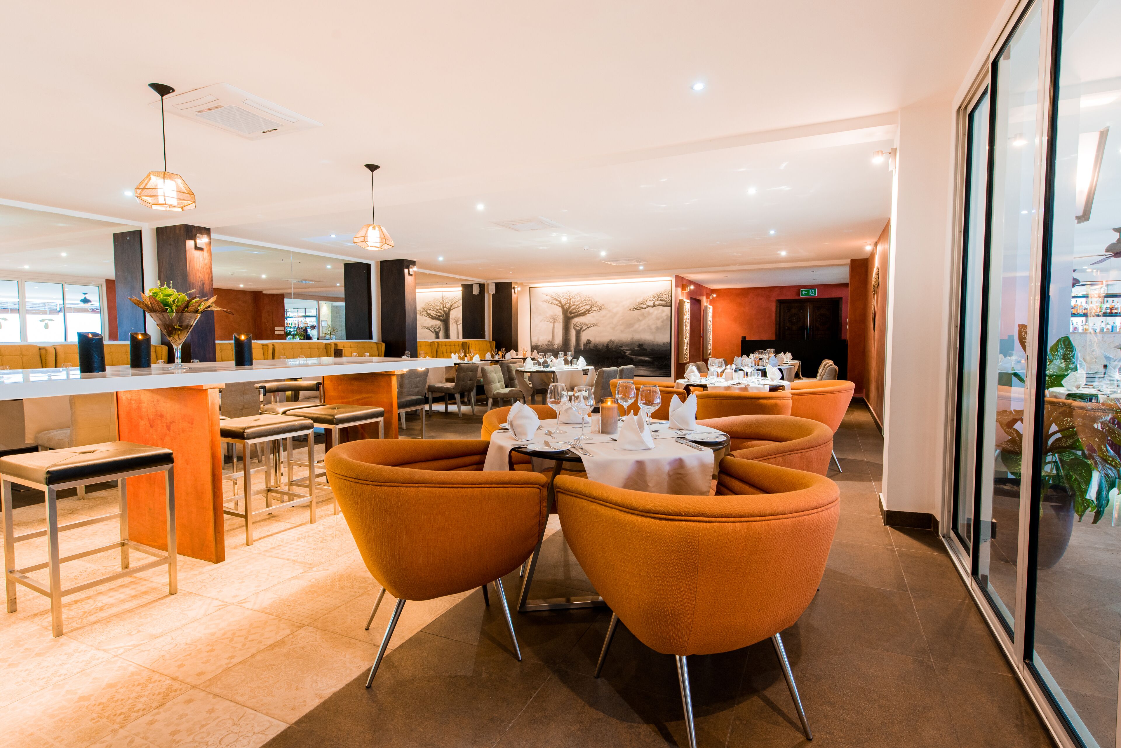 A modern restaurant with orange chairs, white tables, and pendant lighting.