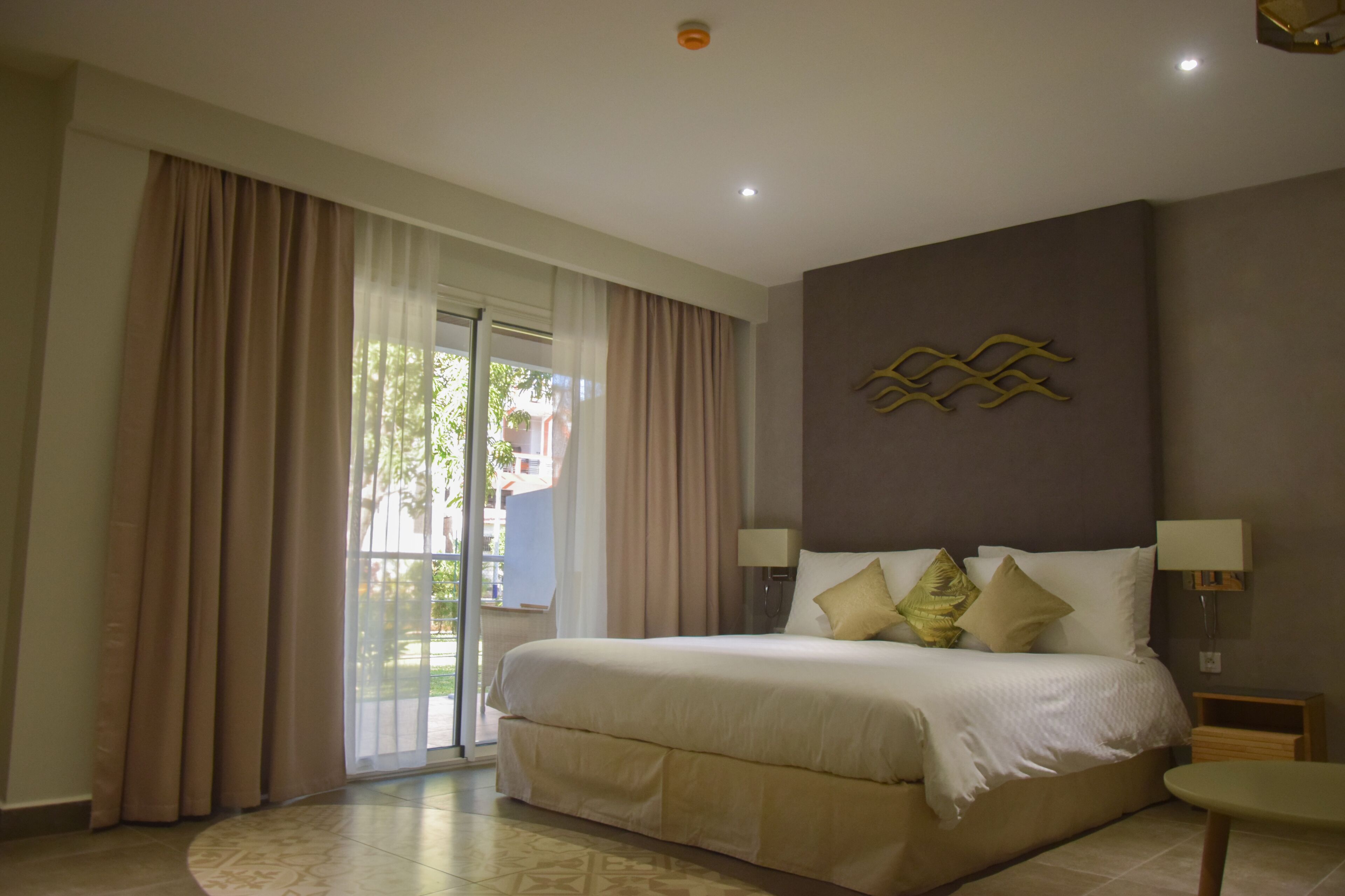 Habitación de hotel con una cama grande, puerta corrediza al exterior y una lámpara fijada a la pared.