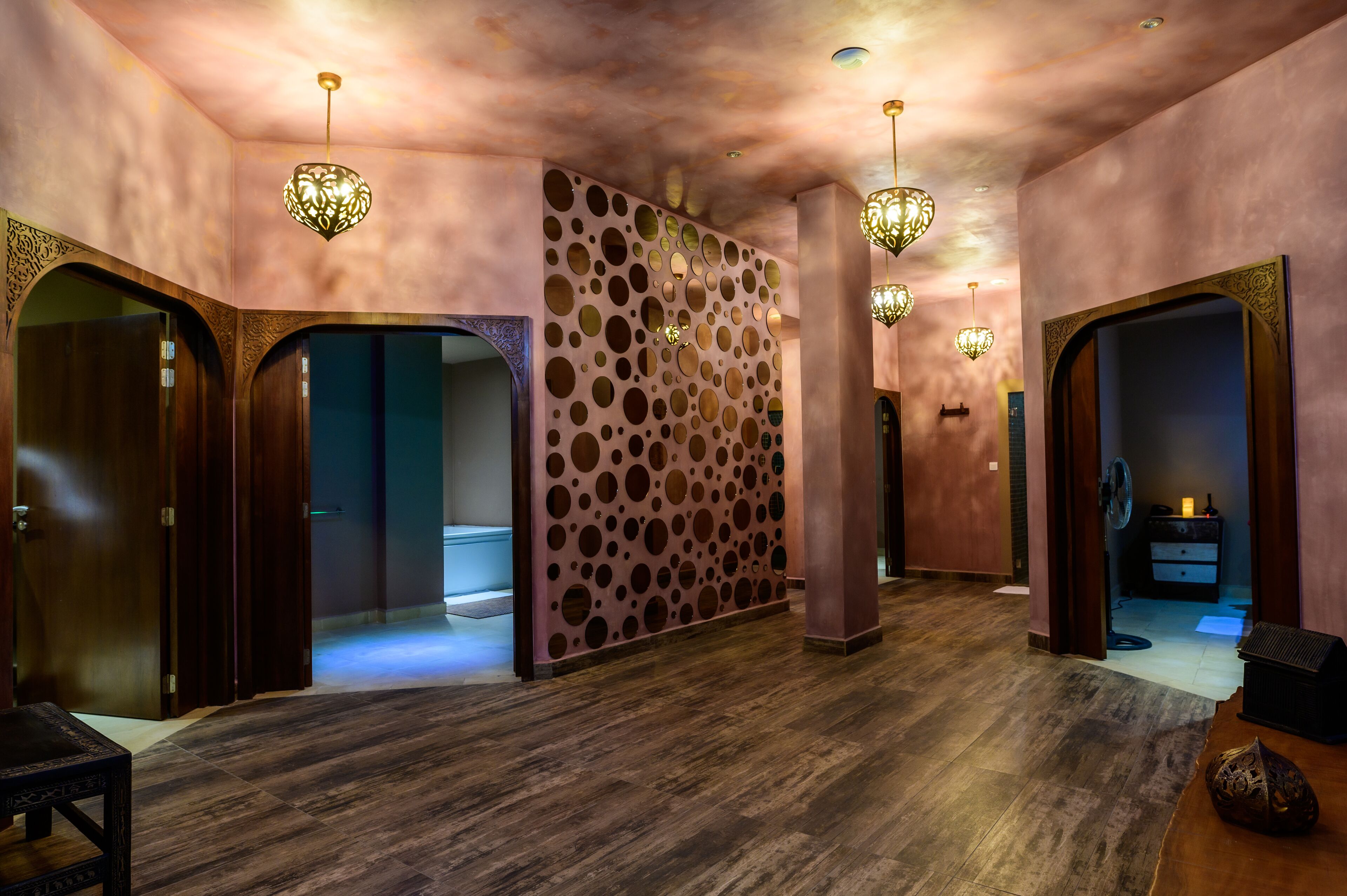 A hallway with wooden flooring, a patterned wall, and multiple doorways leading to different rooms.
