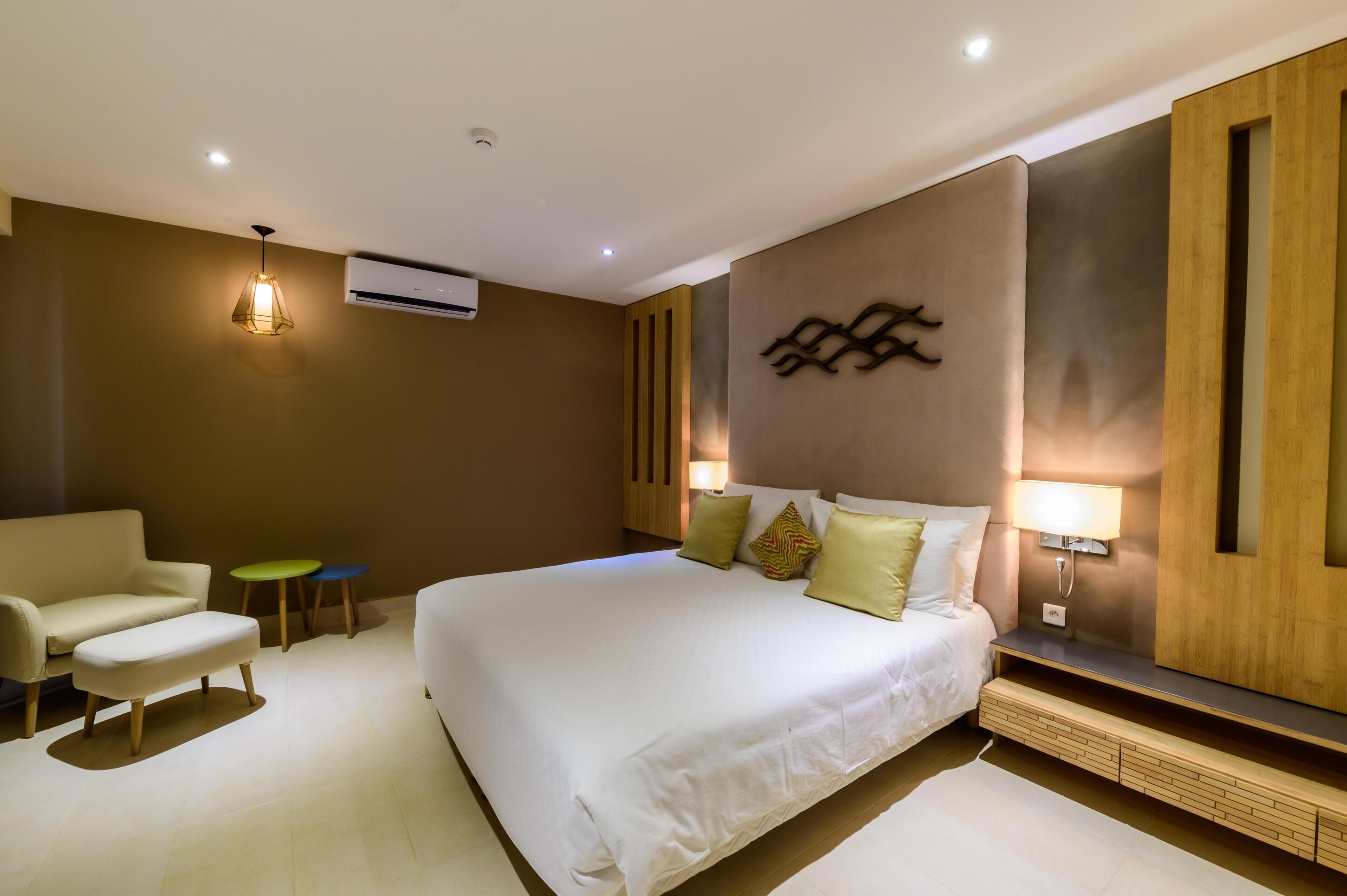 Una habitación de hotel moderna con una cama grande, un sofá, una mesita y aire acondicionado instalado en la pared.