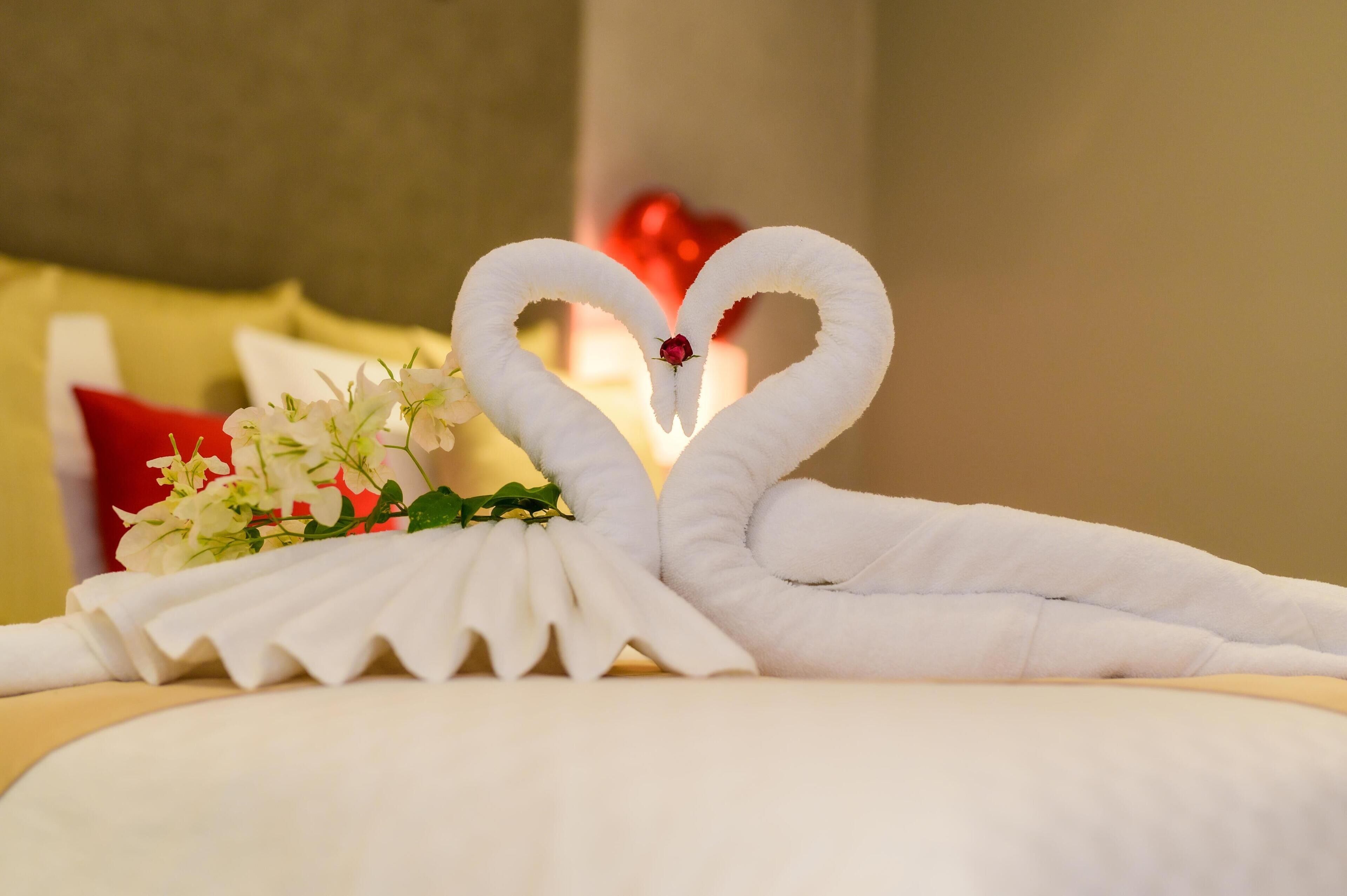 Una cama con una toalla dispuesta en forma de corazón y un pequeño ramo de flores.