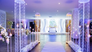 Un salón de bodas con un pasillo blanco, decoración floral y un escenario con fondo decorativo.