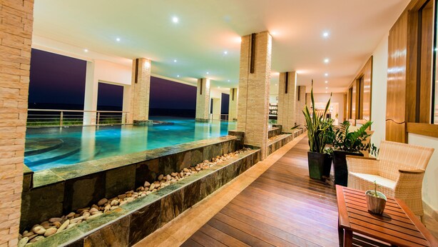 Área de piscina interior moderna con vista al cielo nocturno, suelo de madera y asientos con plantas en macetas.