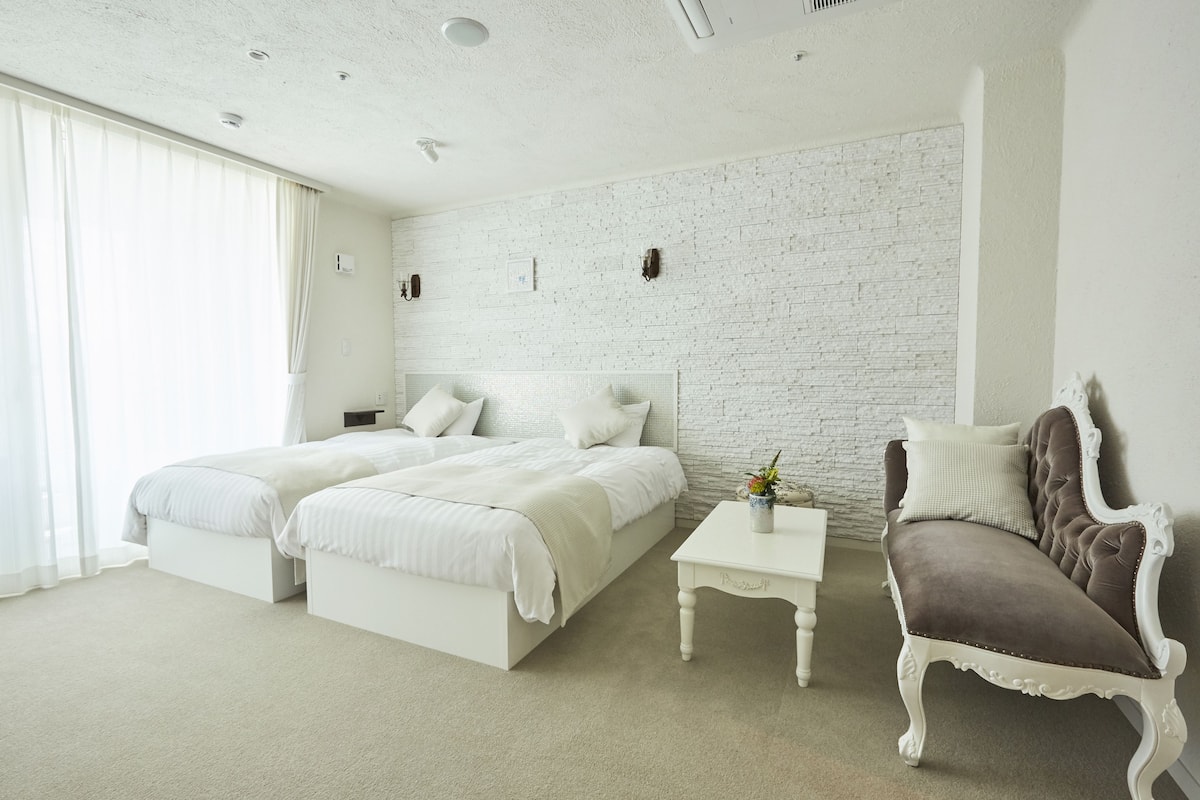 A bedroom with two beds, a white coffee table, and a brown upholstered chair.