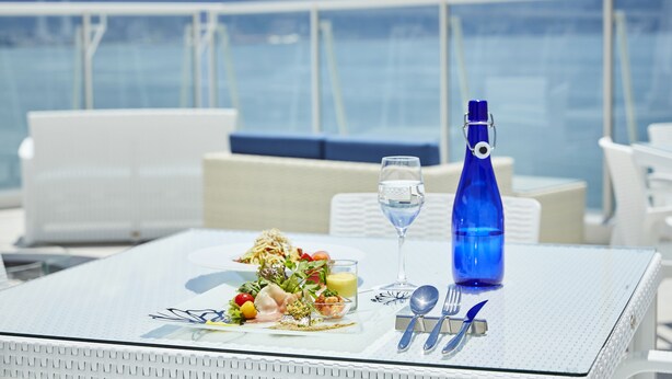 A table set with a meal, a glass of water, and a blue bottle on a balcony with a view of the sea. - Wakanoura Nature Resort Epicharis (Wakayama)