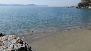 A beach with calm water, a rocky shoreline, and distant mountains under a clear sky. - Wakanoura Nature Resort Epicharis (Wakayama)