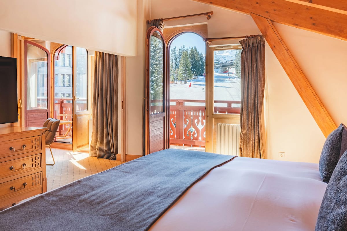 Una habitación de hotel con una cama grande, un aparador de madera y un televisor. Hay cortinas y vistas a un paisaje nevado a través de las ventanas.