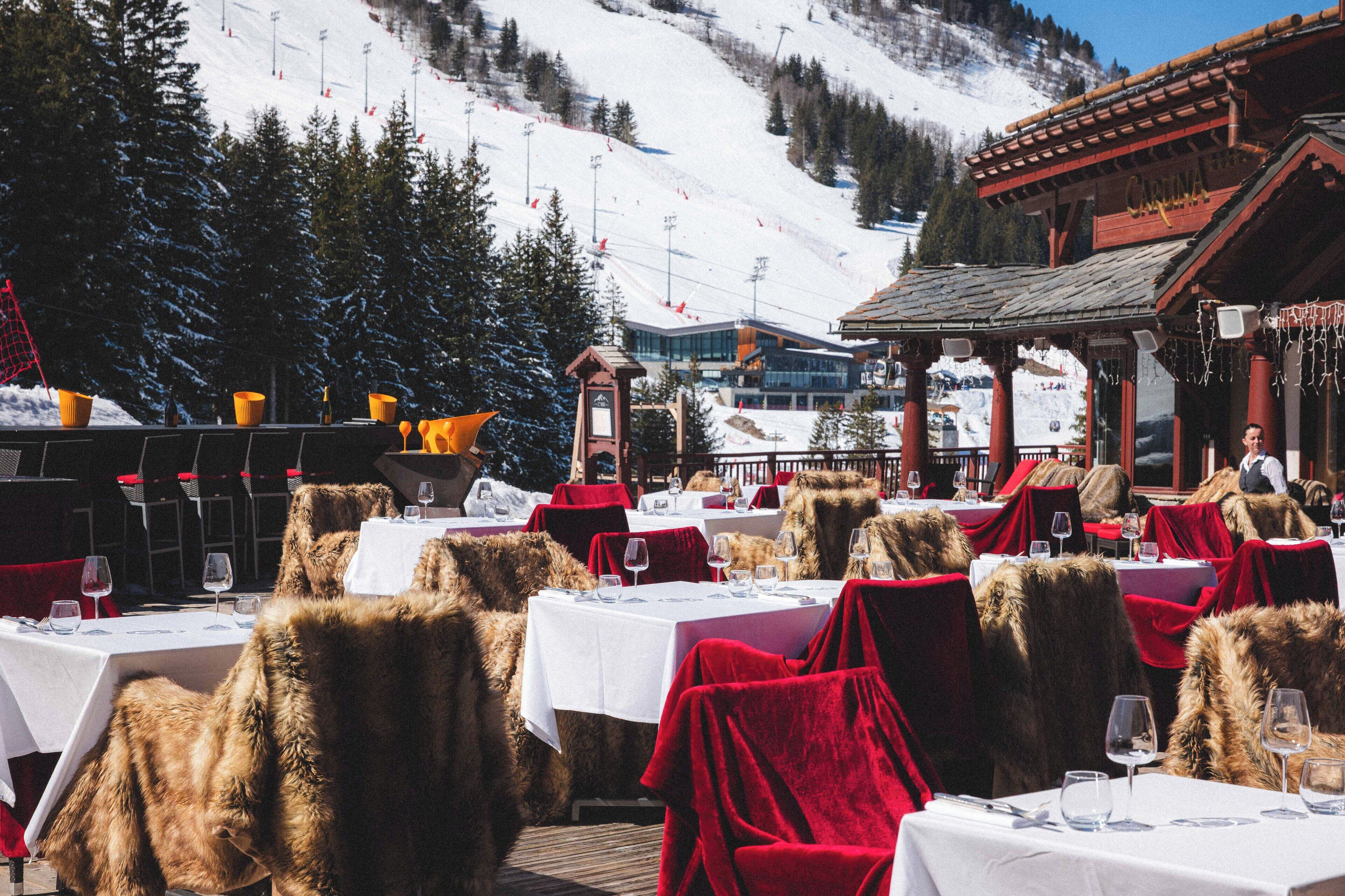 An outdoor dining area with tables set for guests, surrounded by snow-covered mountains and trees.