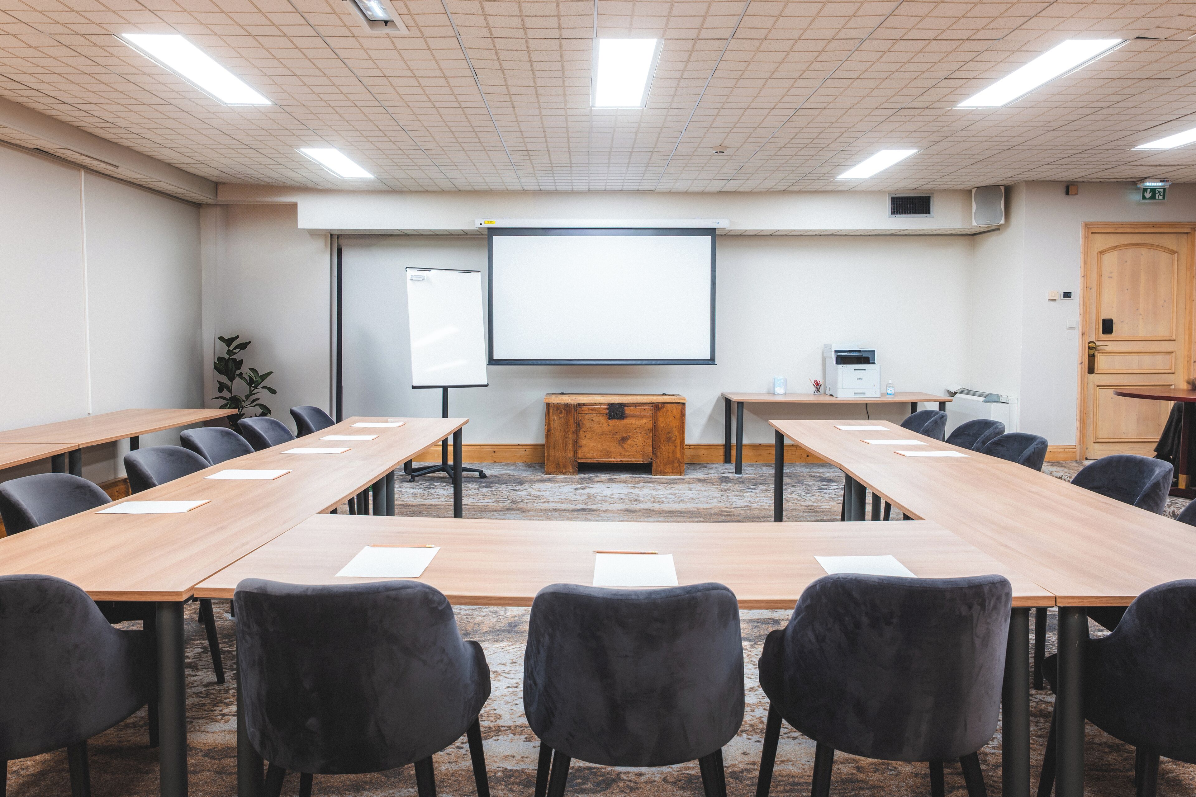 A conference room with long tables, chairs, a projector screen, and a whiteboard.
