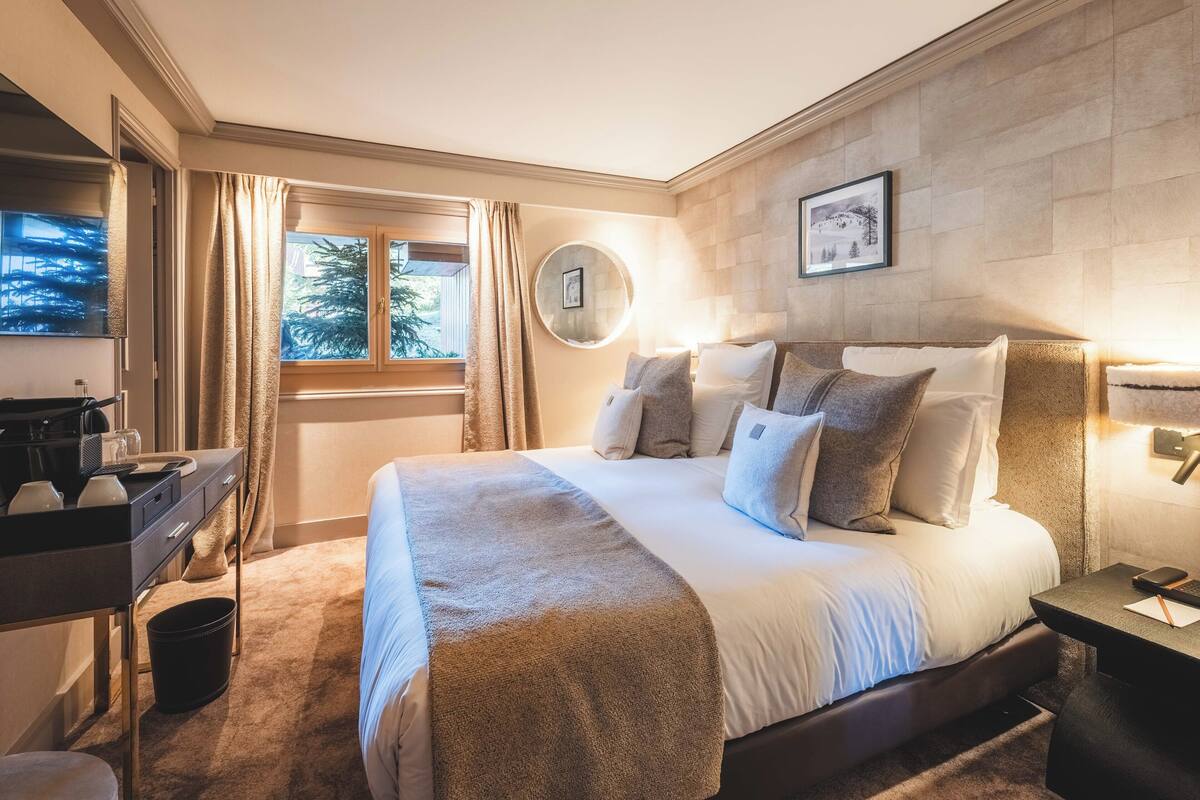 Un dormitorio bien iluminado con una cama grande, un escritorio y una ventana con cortinas.