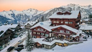 A snow-covered mountain resort with multiple buildings, including a prominent red-roofed structure with balconies and a sign that reads "Carpina."