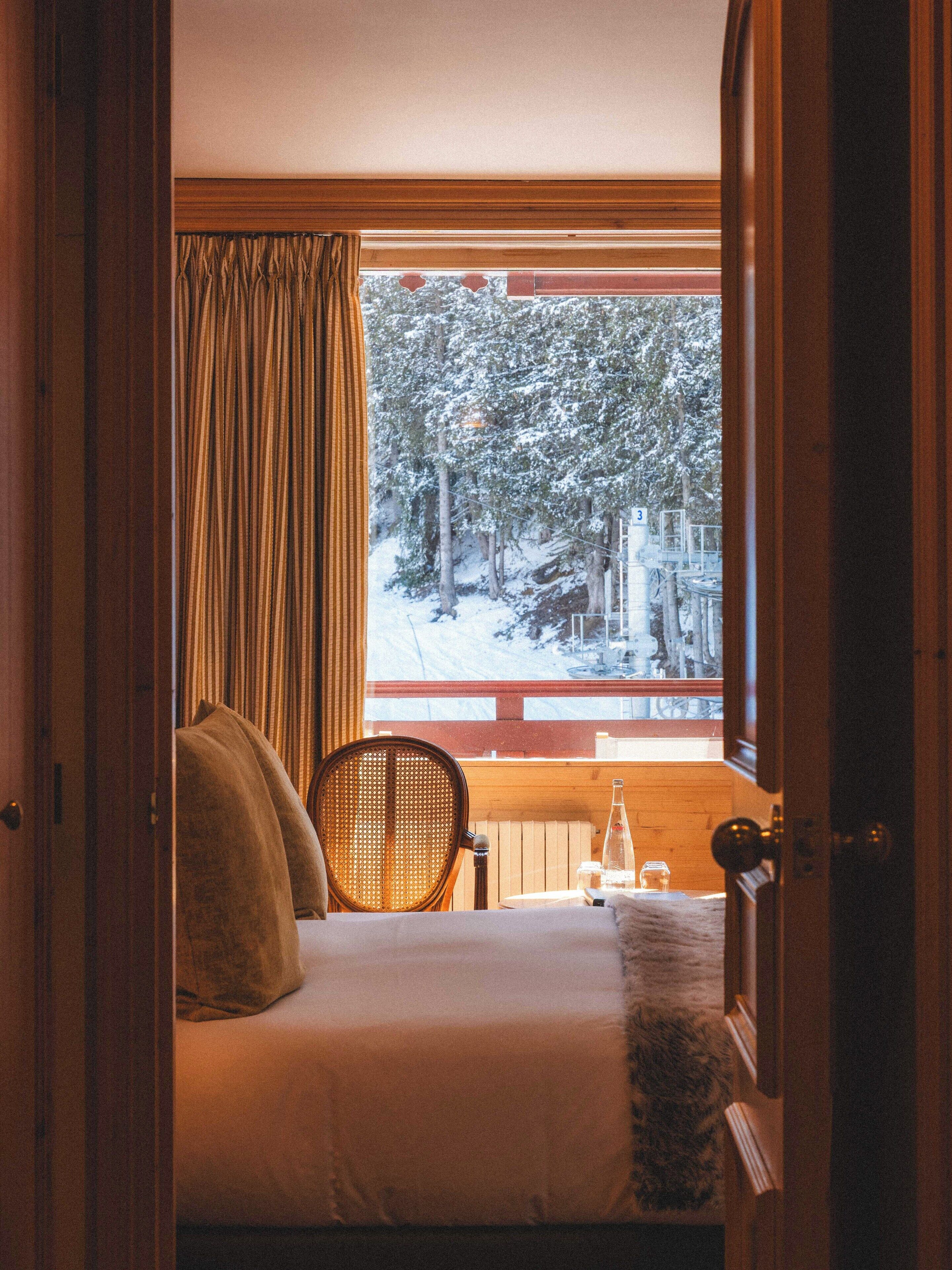 A bedroom with a bed, a chair, a window with a view of a snowy forest, and a wooden railing.