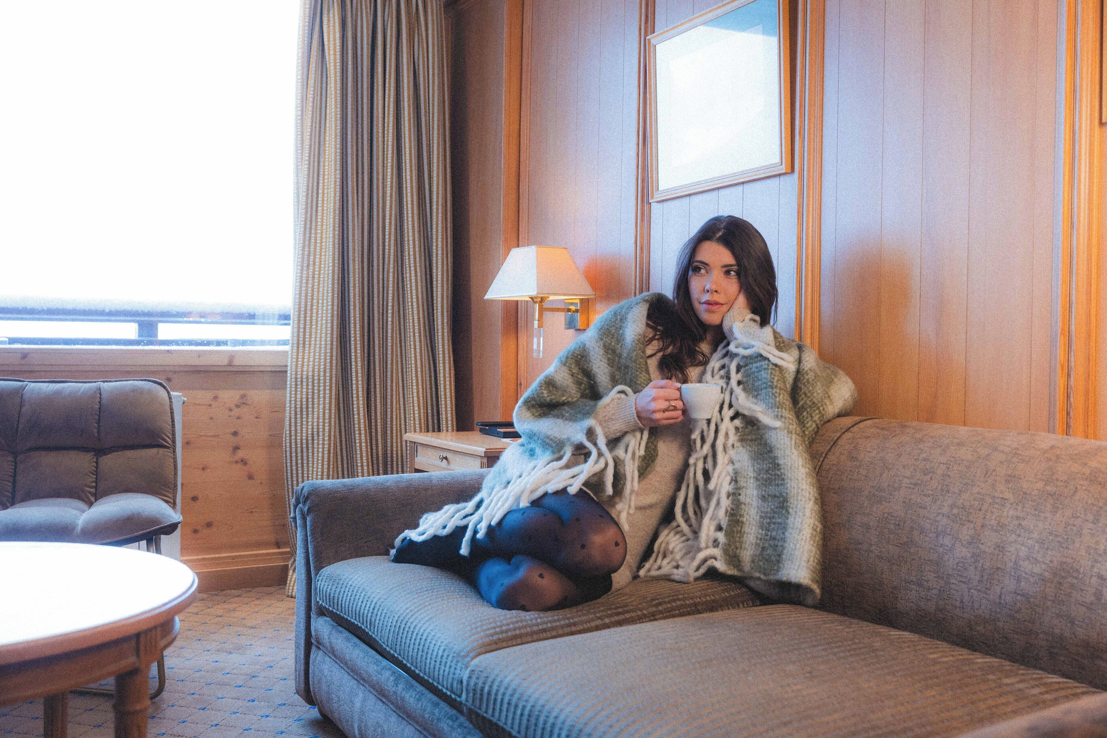 A room with a sofa, a small table, a lamp, and a window with curtains.