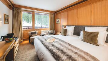 Ett hotellrum med en stor säng, en sänggavel i trä, en stol, ett litet bord och ett fönster med gardiner.