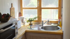 A compact kitchen with wooden cabinets, a built-in oven, a sink, and a window with a view of greenery outside. - Müllers Ferienhaus Gunaras (Dombovar)