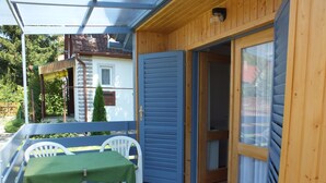 A covered outdoor area with a table and chairs, a wooden door, and a view of the surrounding neighborhood. - Müllers Ferienhaus Gunaras (Dombovar)