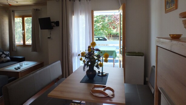 A cozy room with a wooden ceiling, a dining table with a vase of flowers, a sofa, and a television mounted on the wall. - Müllers Ferienhaus Gunaras (Dombovar)
