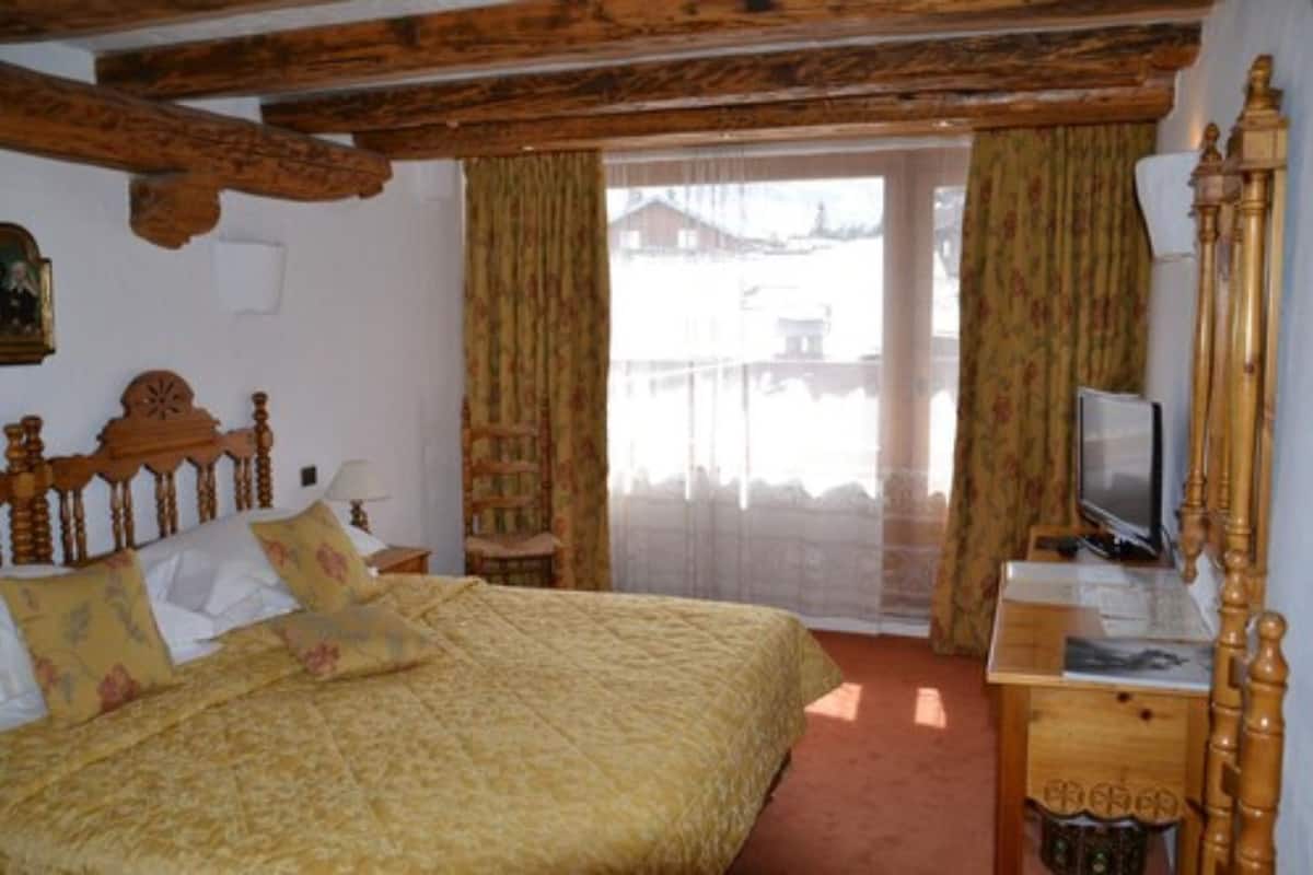 A bedroom with a wooden bed, a television on a wooden dresser, and a window with curtains.