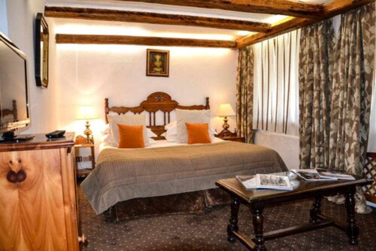 A hotel room with a wooden headboard bed, two bedside lamps, a wooden dresser, and a small table with magazines.