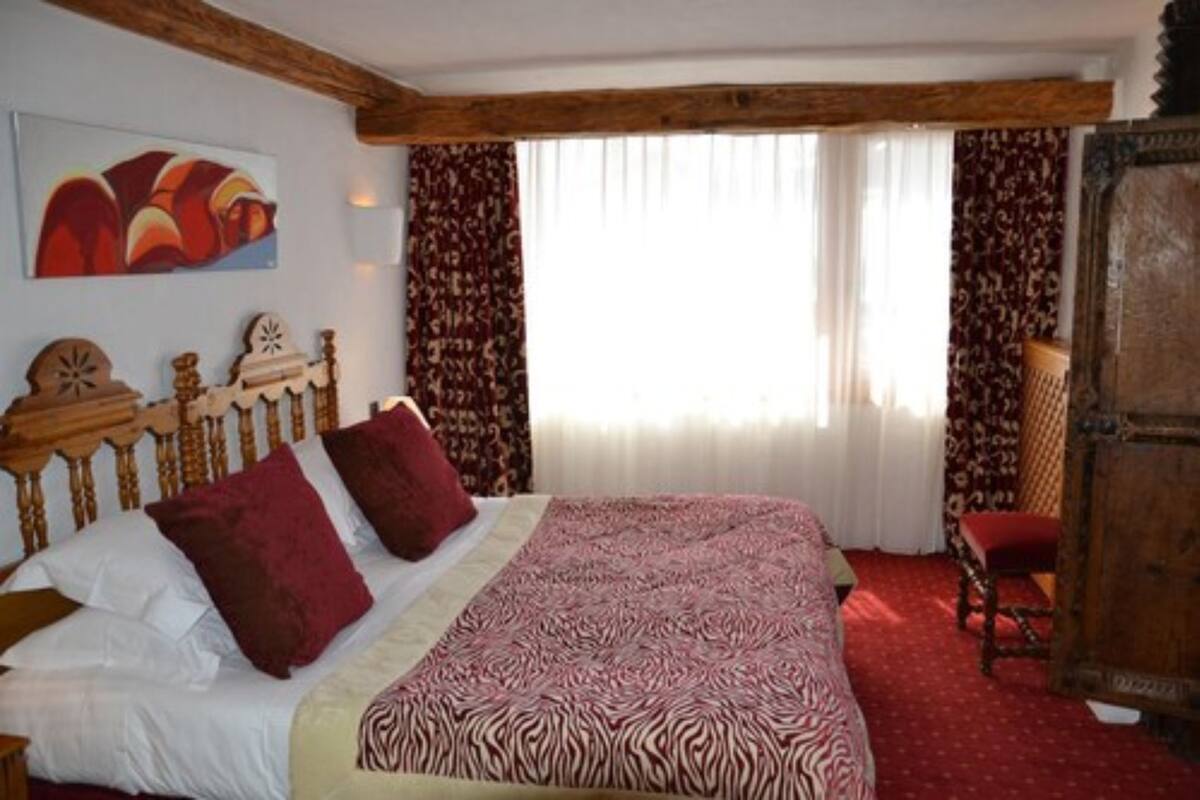 A bedroom with a wooden bed, patterned bedspread, and curtains.