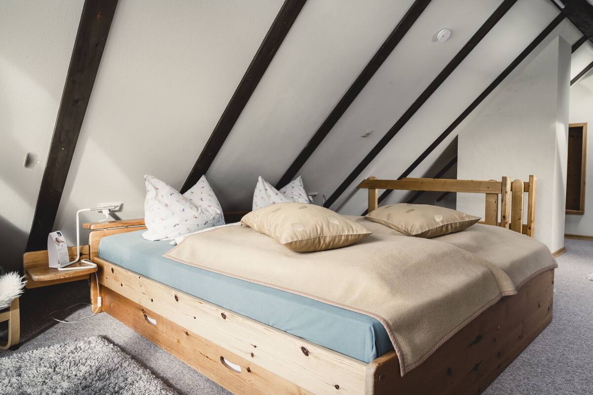 Une chambre avec un plafond en pente, un lit en bois, une table de chevet et une lampe.