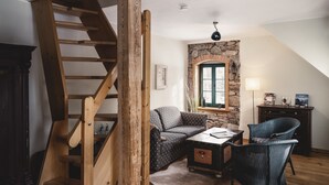 A cozy room with a wooden staircase, a stone wall, a green door, a sofa, a coffee table, and a chair. - Altsächsischer Gasthof Kleines Vorwerk (Sayda)