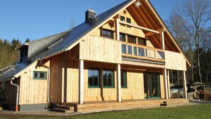 A two-story wooden cabin with a sloped roof, large windows, and a covered porch. - Altsächsischer Gasthof Kleines Vorwerk (Sayda)