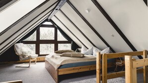A cozy attic bedroom with a sloped ceiling, a wooden bed, a chair, and a large window providing natural light. - Altsächsischer Gasthof Kleines Vorwerk (Sayda)