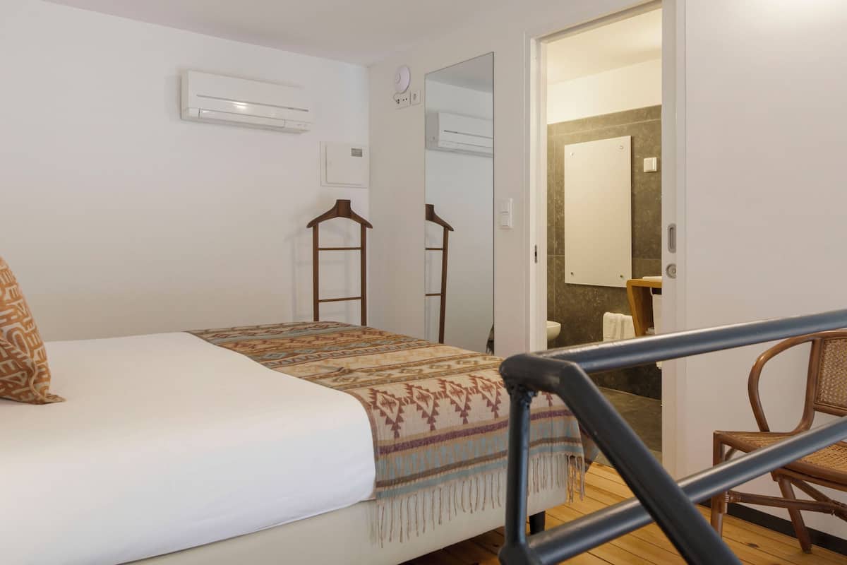 Une chambre à coucher avec un lit, un plancher en bois, une chaise et une porte donnant sur une salle de bain.
