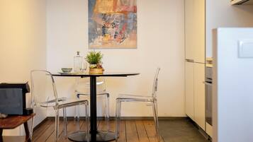 A modern kitchen with a round table, clear chairs, and a painting on the wall.