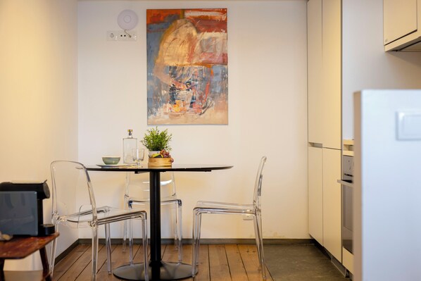 Une cuisine moderne avec une table ronde, des chaises transparentes et un tableau accroché au mur.