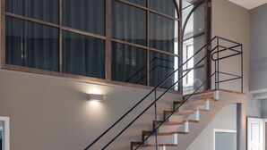 Ein modernes Interieur mit einer Holztreppe, einem grünen Sofa und einem großen Fenster mit Vorhängen.