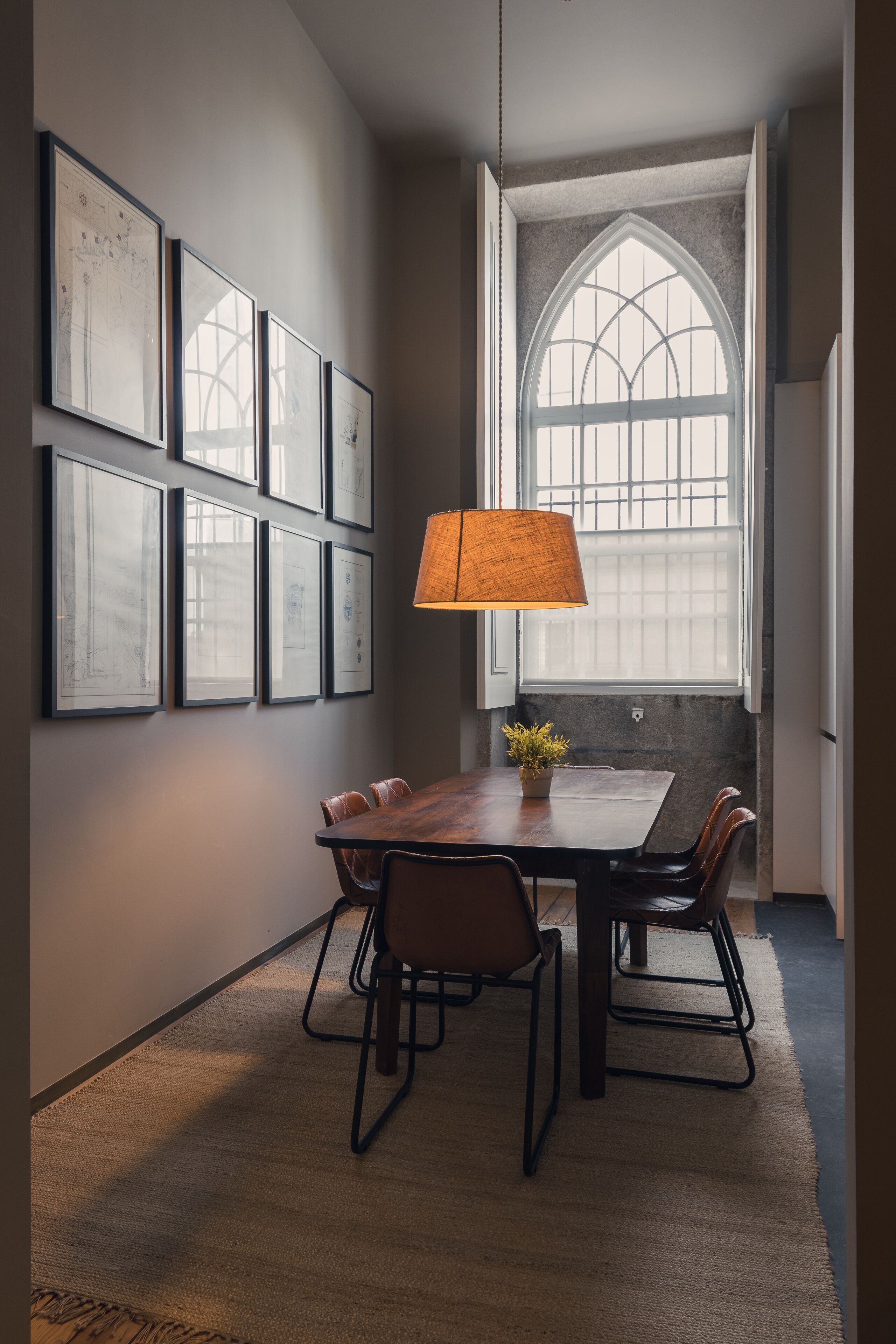 A dining area with a table, chairs, a lamp, and framed artwork on the wall.