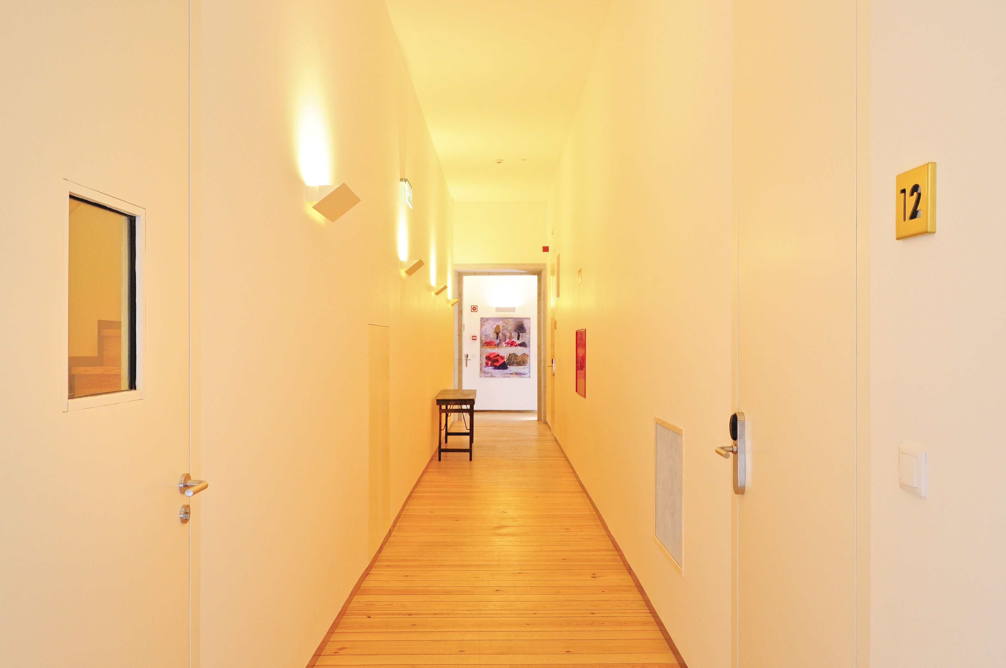 A hallway with a wooden floor, a bench, and a door with a number sign.