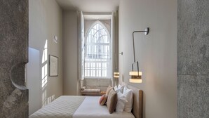 Ein Schlafzimmer mit Bett, einem Fenster mit Gitterstäben, einer Wandleuchte und einer Steinwand.