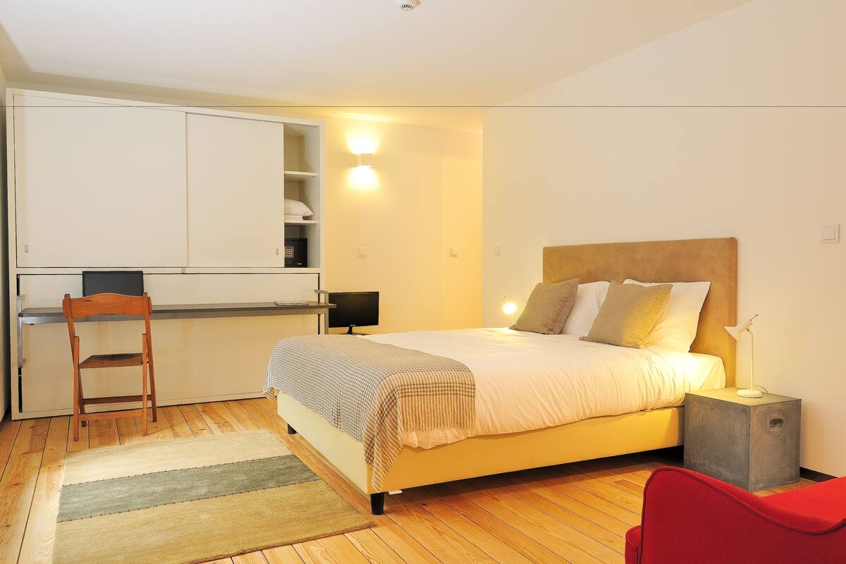 Une chambre à coucher comprenant un lit, une table de chevet, une chaise et un petit coin bureau avec une chaise et une lampe.
