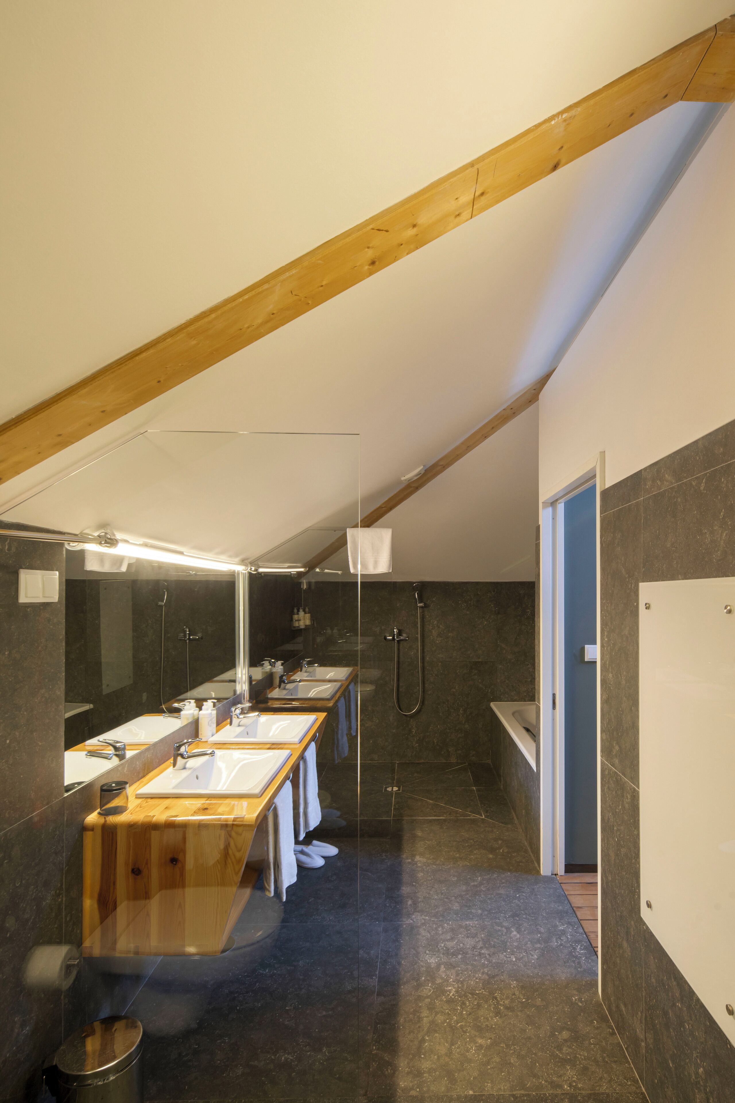 Un baño moderno con techo de madera, paredes de baldosas oscuras y un tocador amplio con varios lavamanos.
