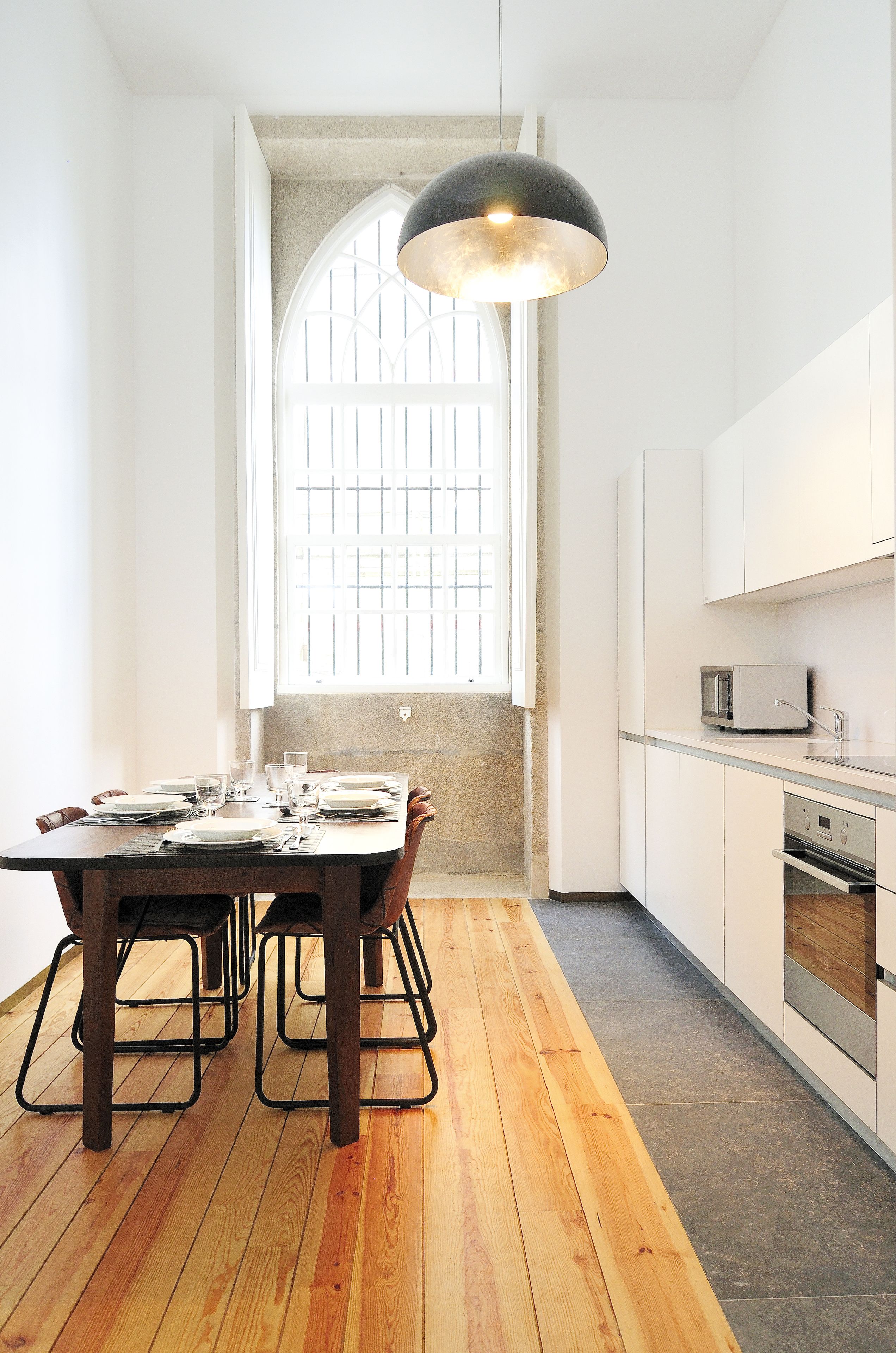 Una cocina moderna con una mesa de comedor para cuatro, un amplio ventanal con barandillas y una lámpara colgante negra.