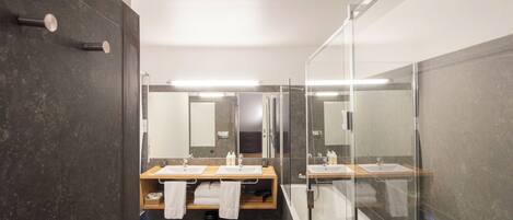 A modern bathroom with a glass-enclosed shower, two sinks, and a mirror.
