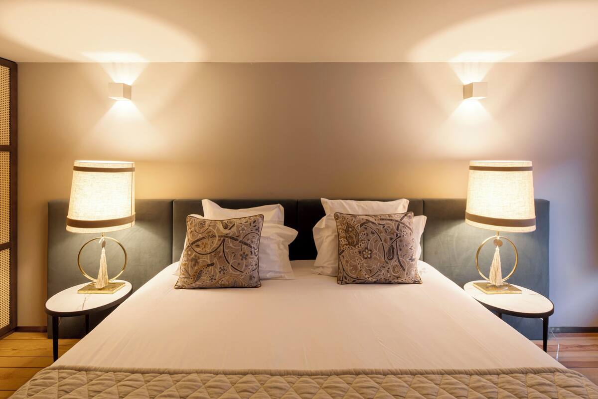 Un lit bien fait, avec deux lampes de chevet, une tête de lit et une couvre-lit matelassé.