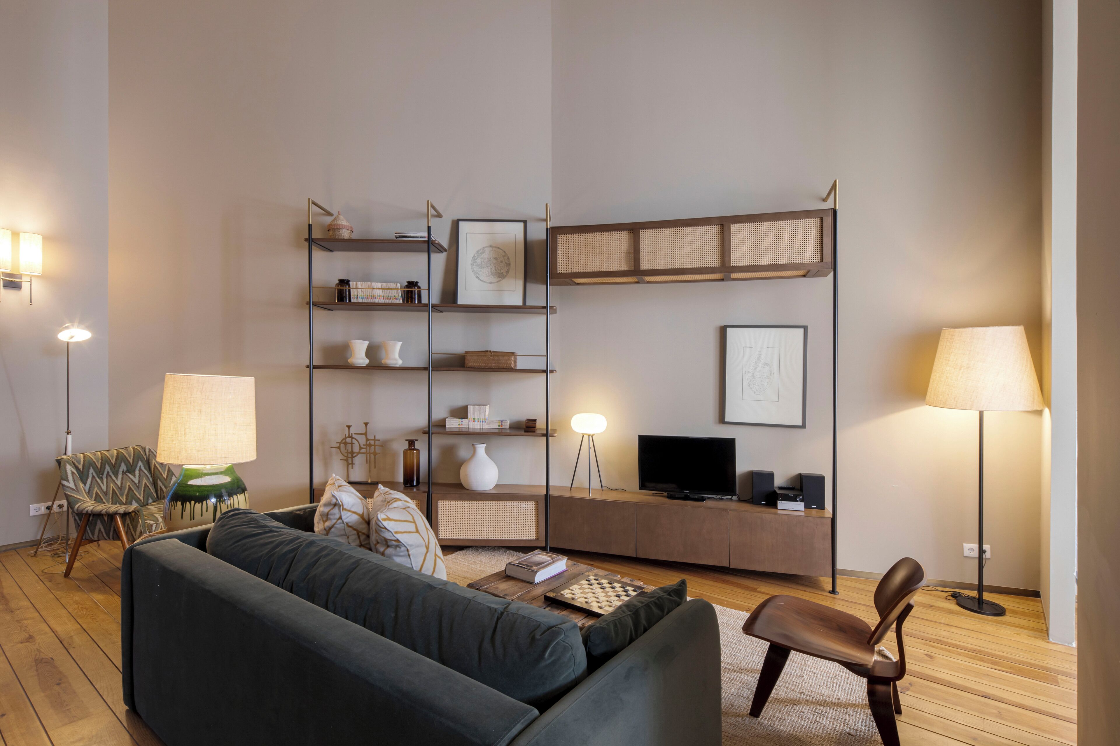 Een moderne woonkamer met een bank, een fauteuil, een salontafel, een boekenkast, een televisie en twee vloerlampen.
