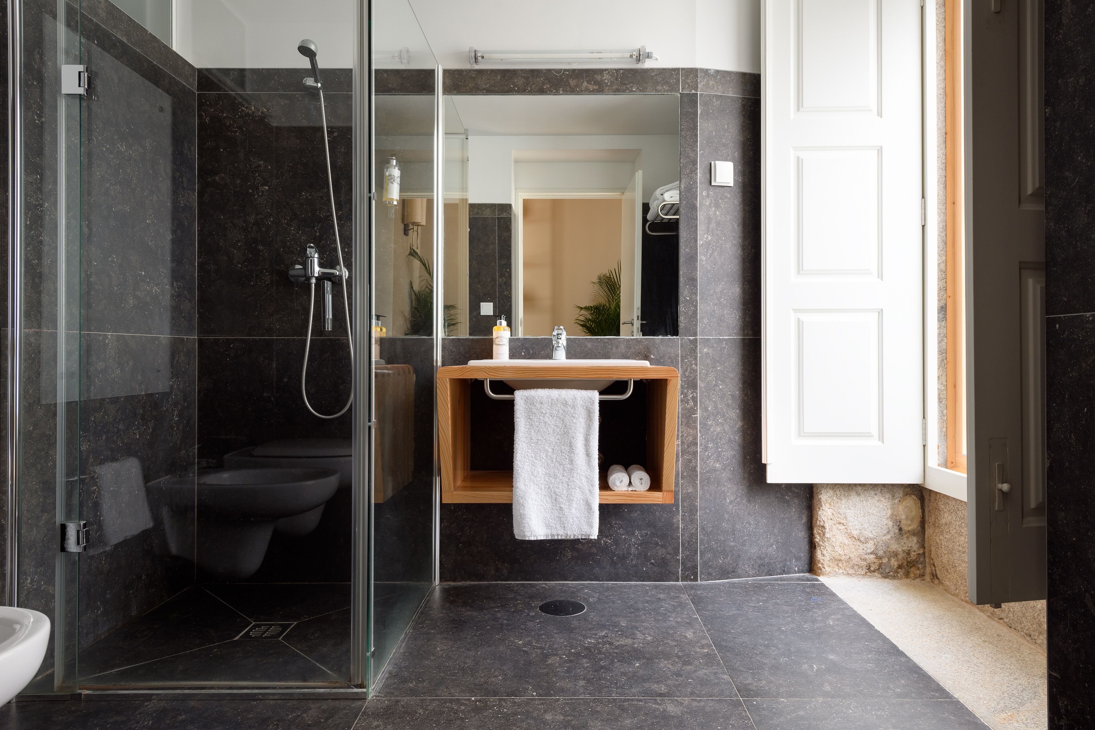A modern bathroom with a glass-enclosed shower, a toilet, and a sink with a wooden shelf.