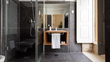 A modern bathroom with a glass-enclosed shower, a toilet, and a sink with a wooden shelf.