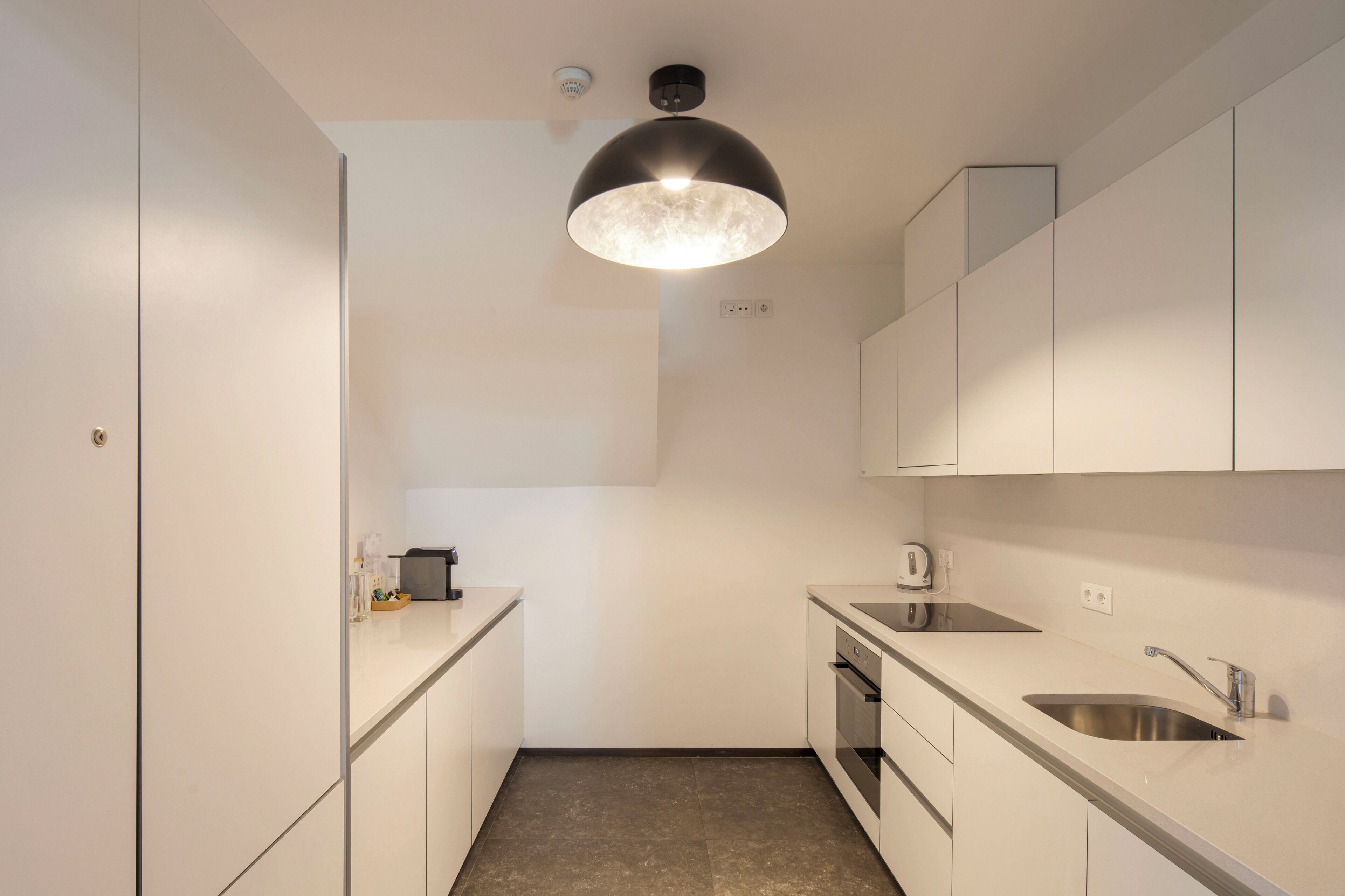 Een moderne keuken met witte kastjes, roestvrijstalen apparatuur en een hanglamp.