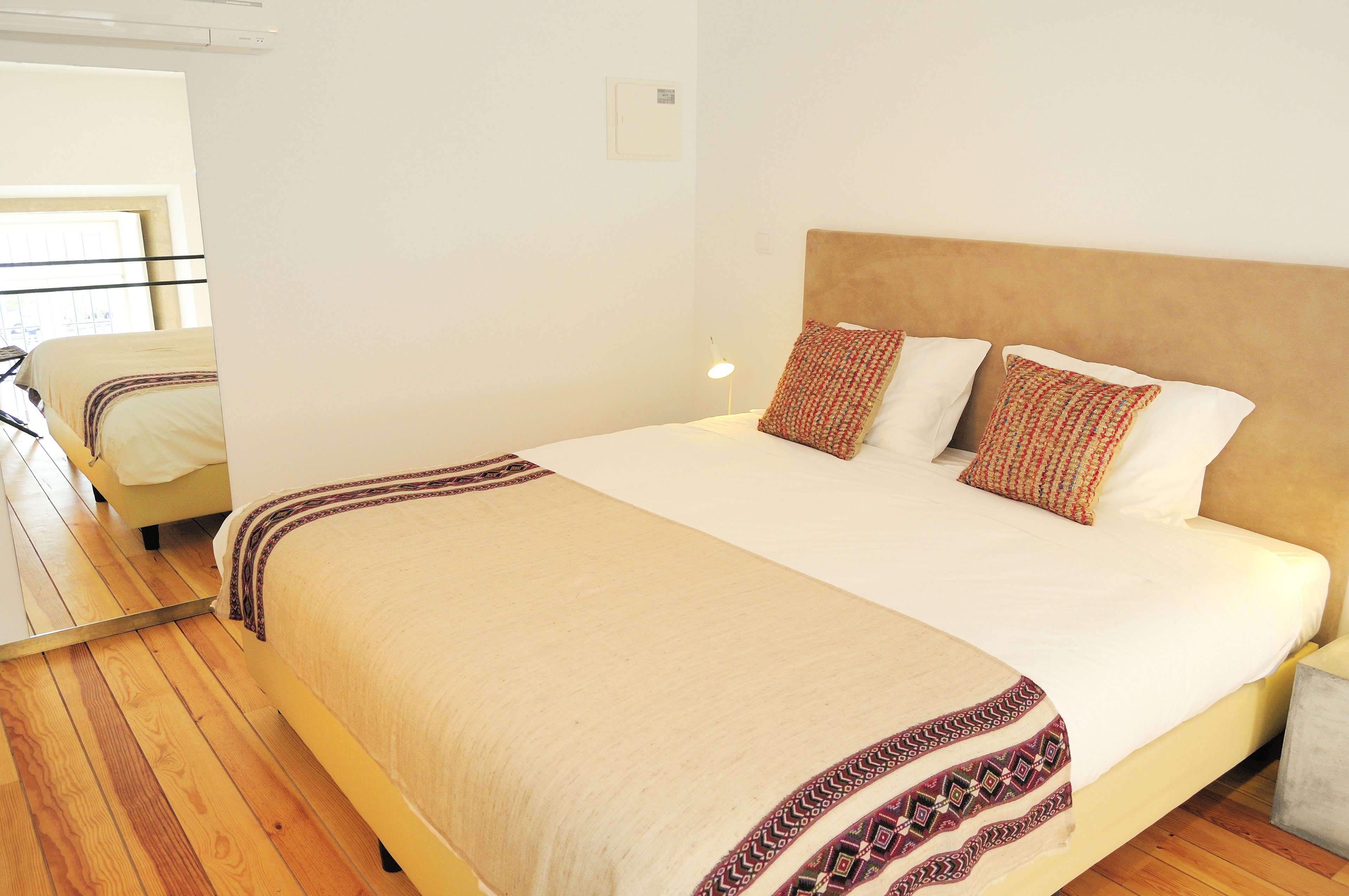 A neatly made bed with a patterned throw, a bedside lamp, and a wooden floor.