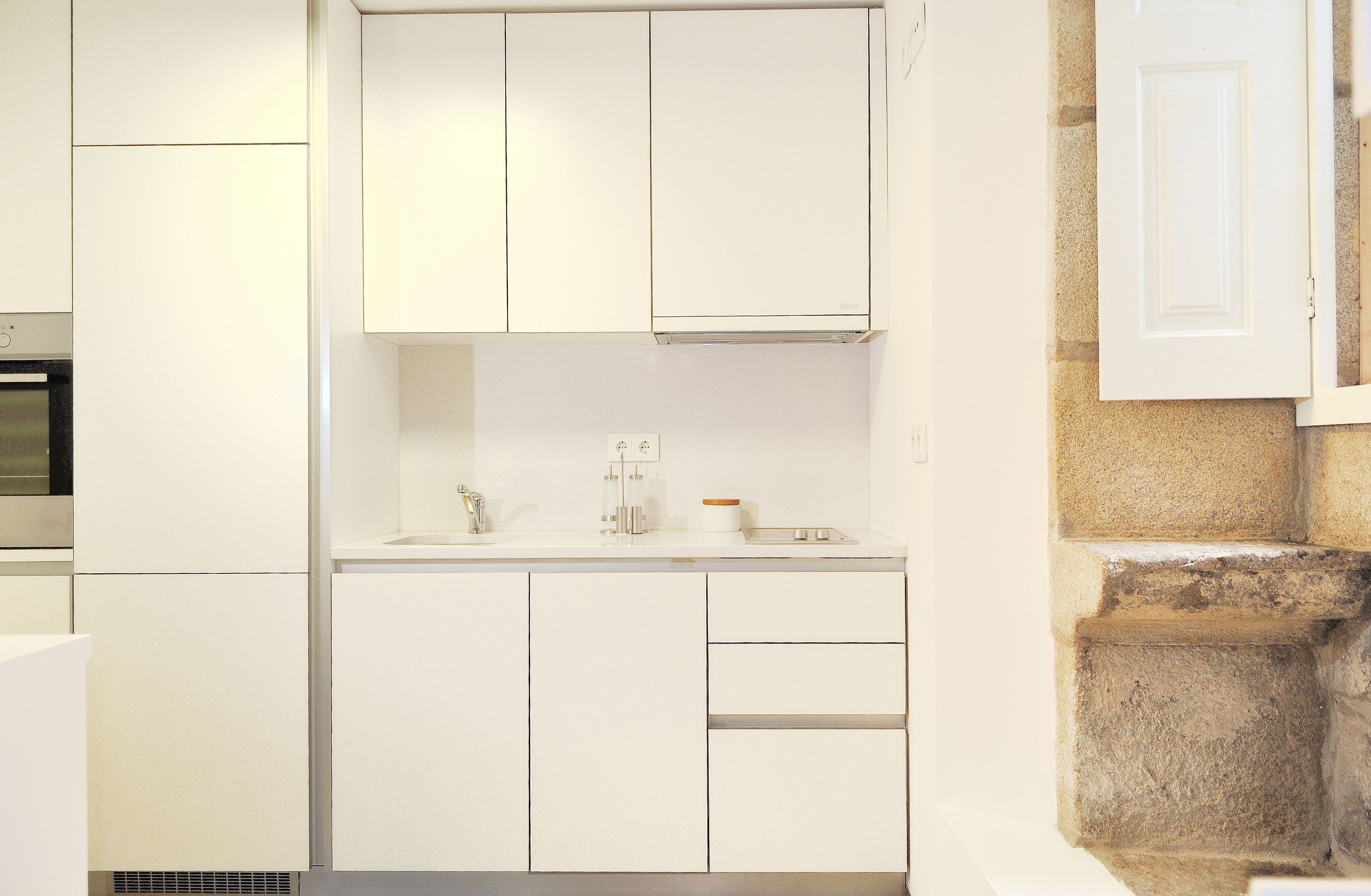 Una cocina moderna con armarios blancos, horno empotrado y pared de piedra.