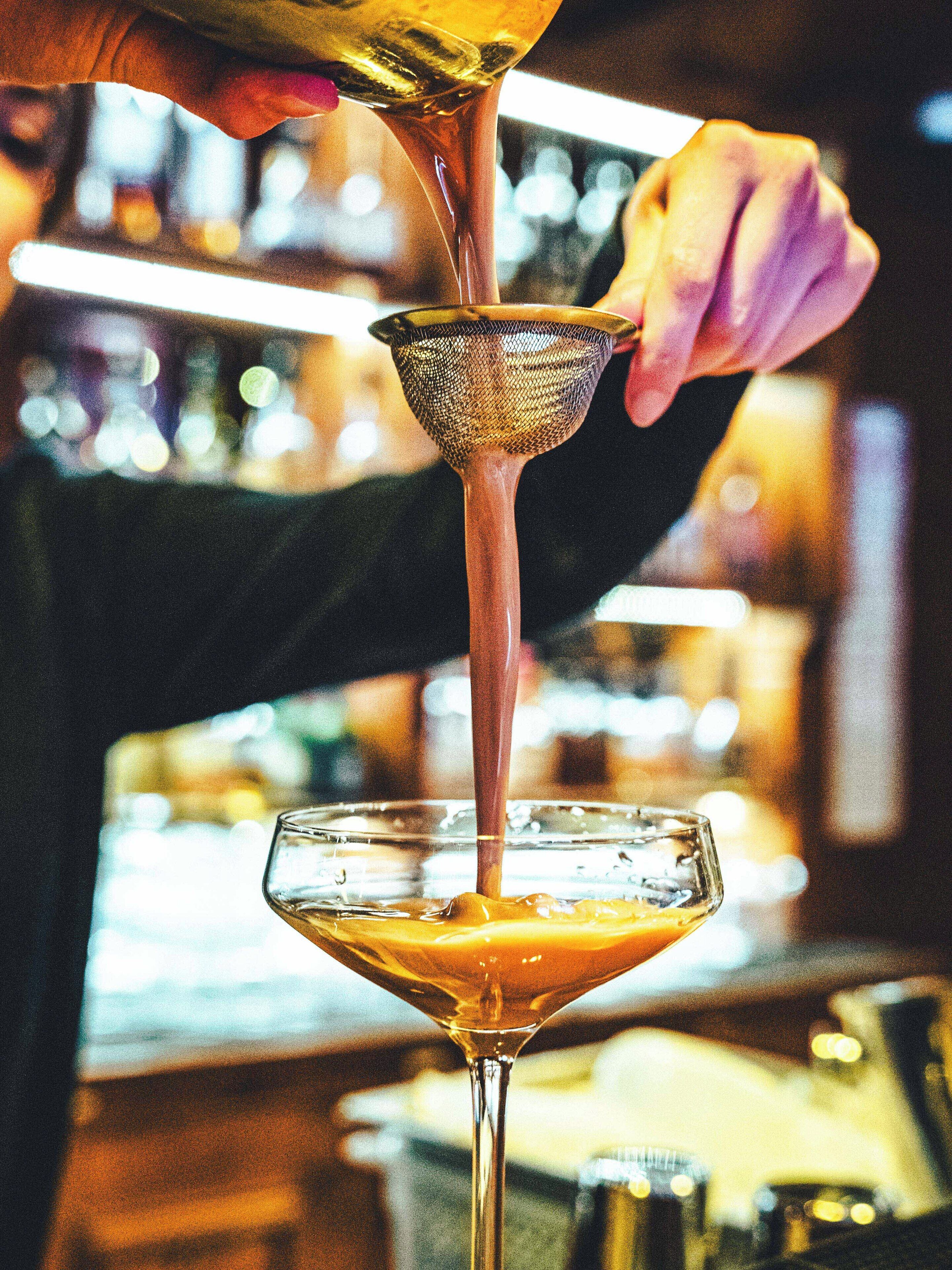 A bartender pouring a drink into a martini glass using a strainer.