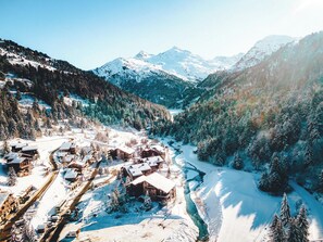 Un pueblo cubierto de nieve en la montaña, con cabañas de madera y un río sinuoso.